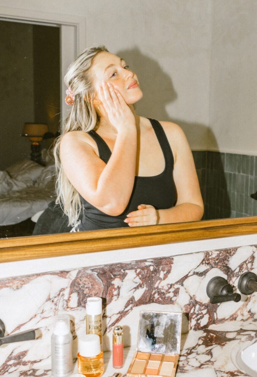 Woman washing her face with skin care products in the mirror.