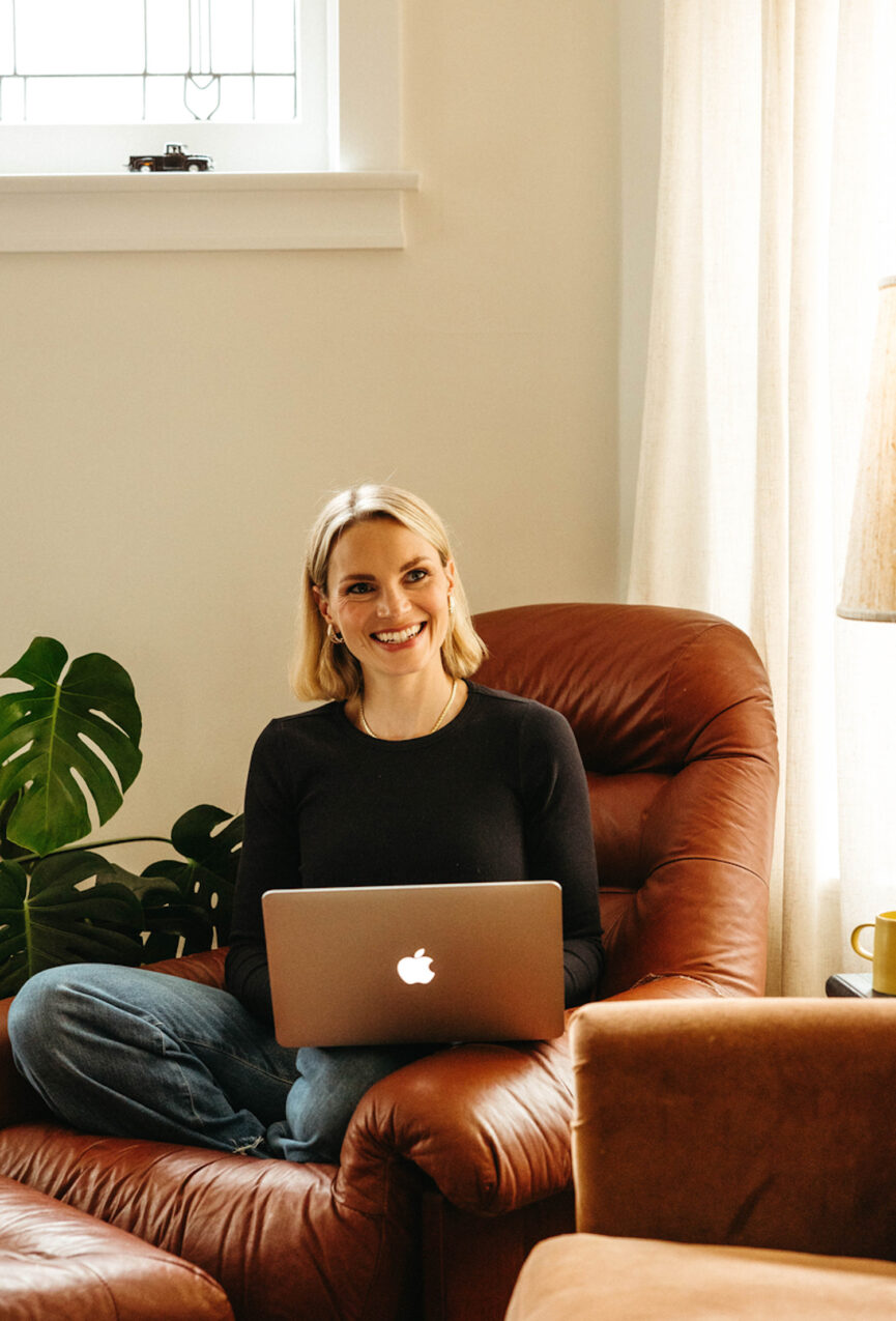 Woman working on laptop in cozy armchair.