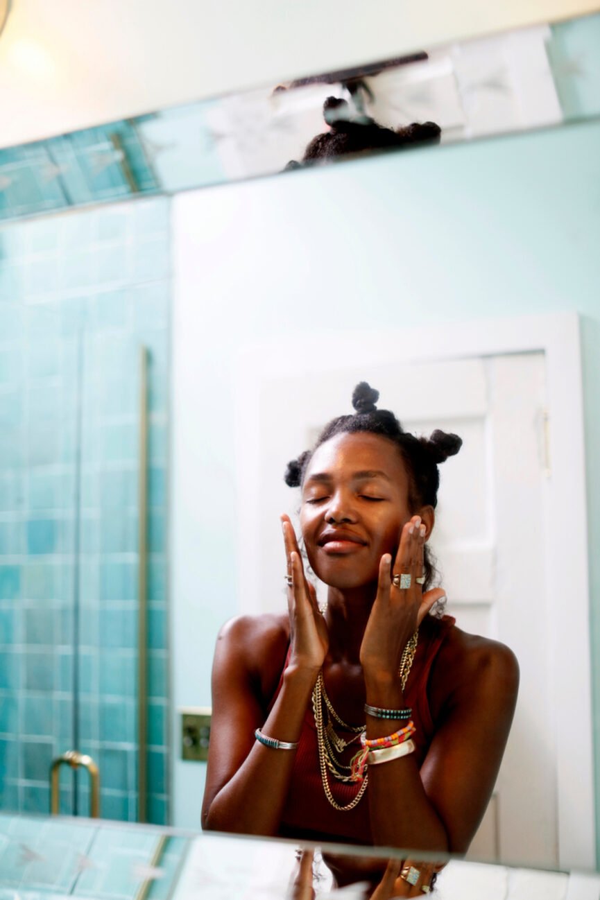 Woman washes face in front of mirror.