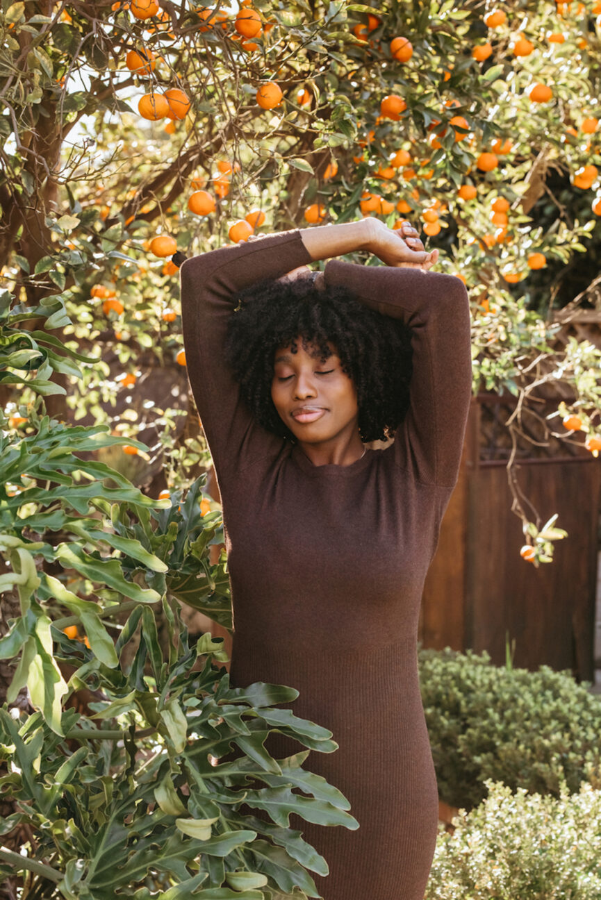 Woman in brown dress posing under orange tree.