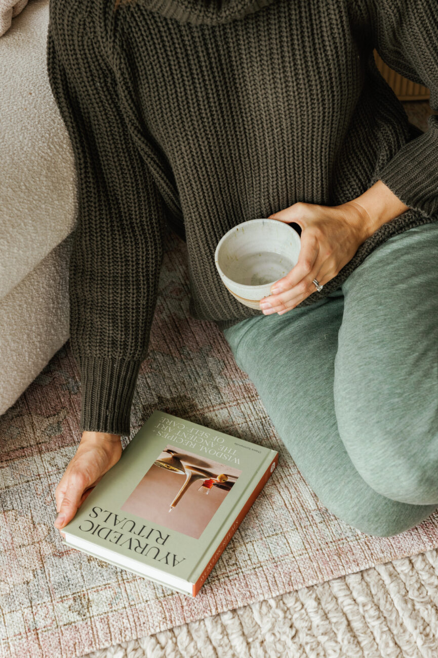 Camille holding a coffee cup in one hand and a book on the floor in another.