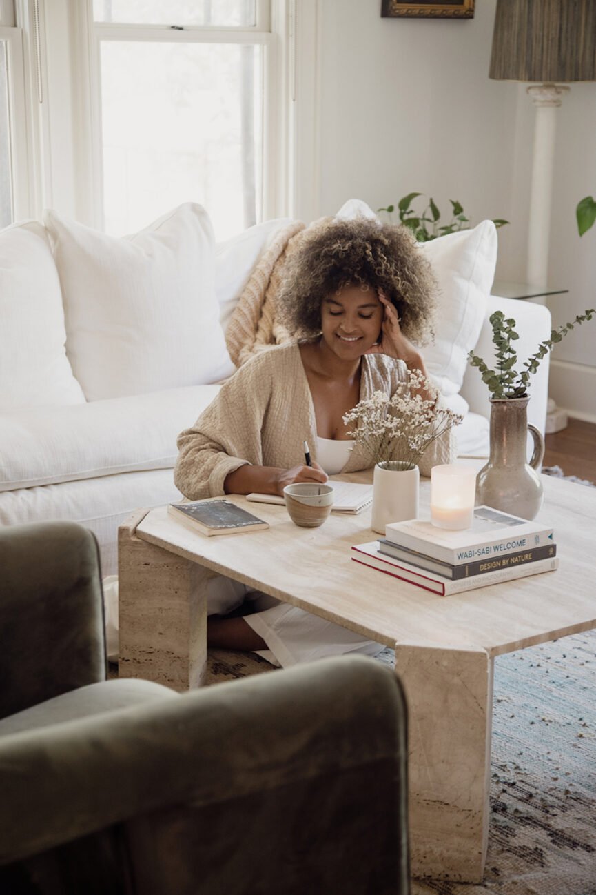 Woman journaling at coffee table in living room.