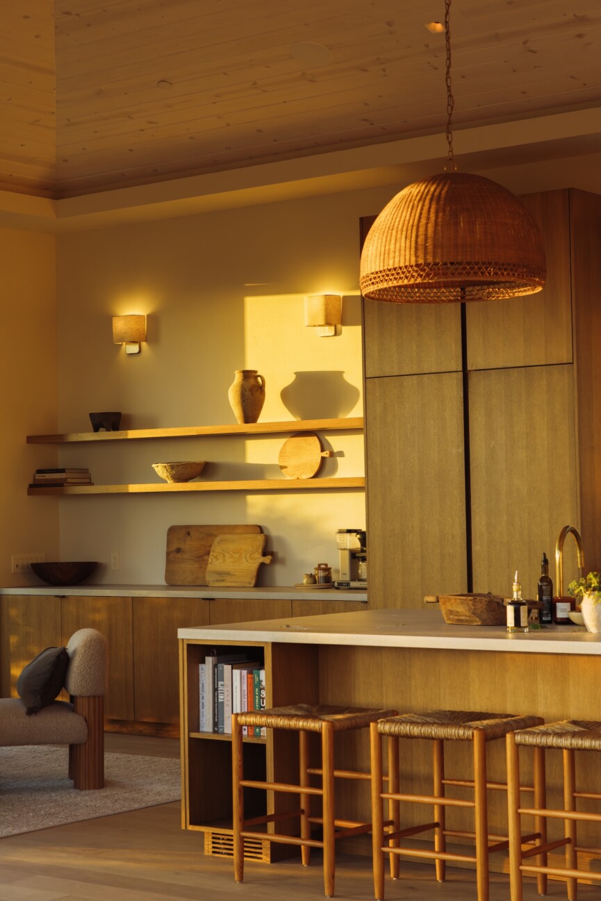 Camille Styles' Malibu great room at dusk, featuring an oak kitchen island, wood cabinetry and woven pendant lights.
