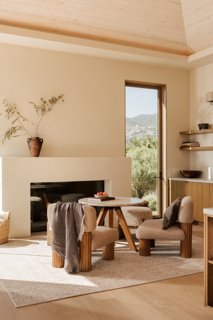 Fireplace seating area in Camille Styles’ Malibu great room with a sculptural wood table, upholstered chairs and mountain views.