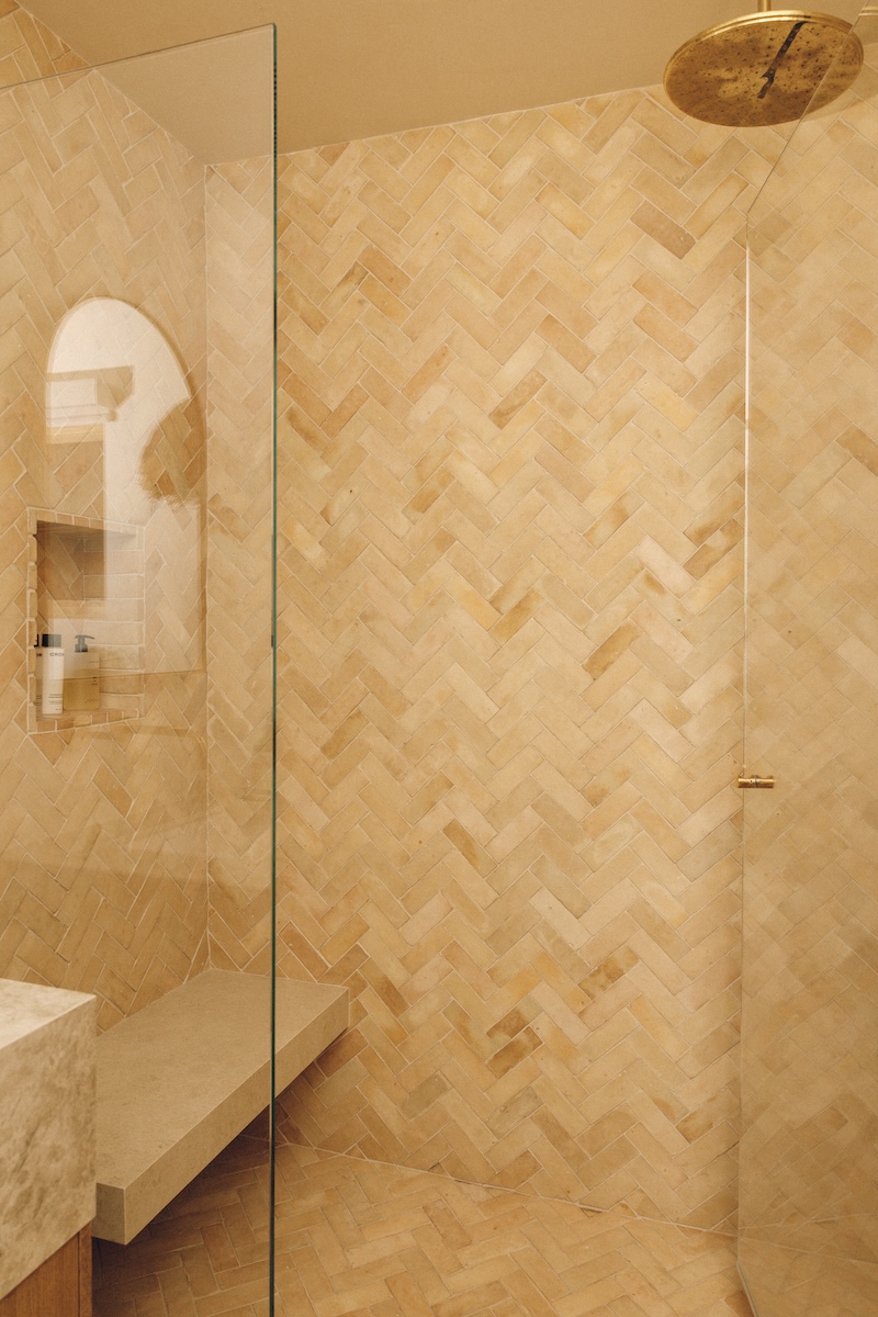 Glass-enclosed shower with warm stone tile laid in a herringbone pattern in the boys’ bathroom.