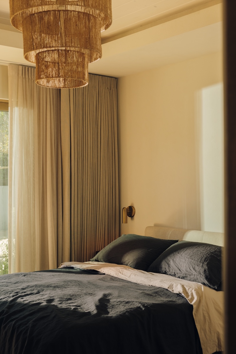 Neutral boys’ bedroom with dark linen bedding, floor-to-ceiling curtains, and a woven ceiling light.