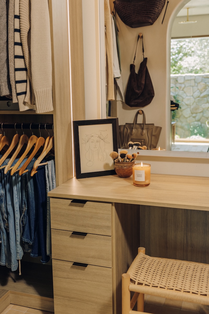 Built-in dressing vanity with wood drawers and a woven stool in Camille Styles’ walk-in closet.