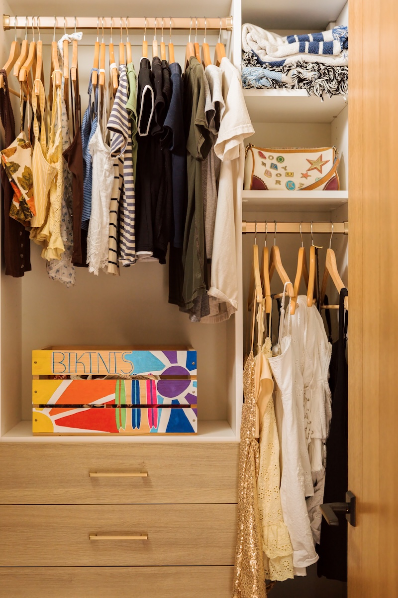 Organized kids’ closet with wood drawers, hanging clothes, open shelving, and colorful artwork.