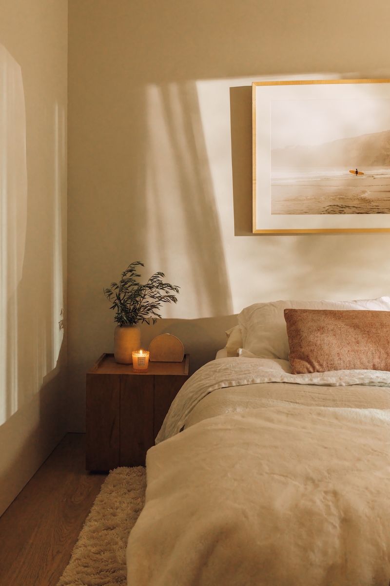 Neutral linen bedding and a wood nightstand styled with a small lamp in Camille Styles’ daughter’s bedroom.