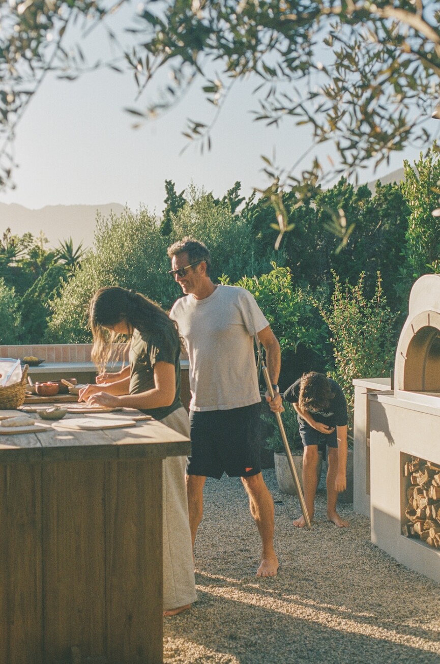 Camille Styles’ family prepares a meal together around the island in their Malibu outdoor kitchen.