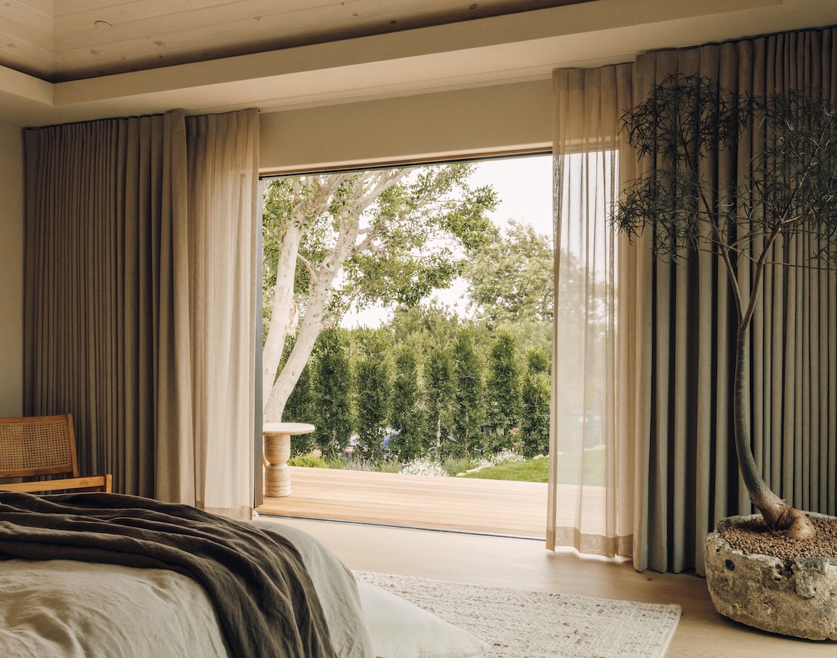 Malibu bedroom with floor-to-ceiling drapes and sheer curtains framing an open doorway to the garden.