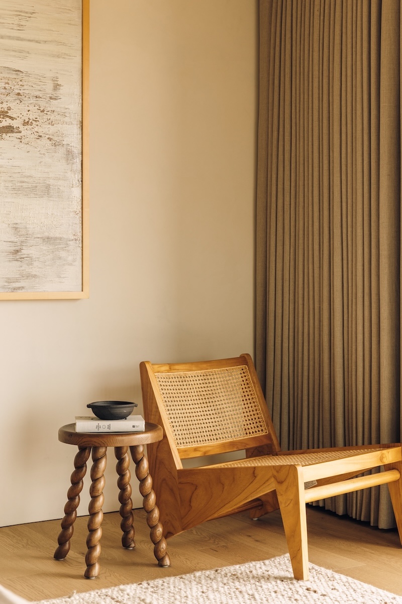Wood and woven reading chair beside a sculptural side table in Camille Styles’ Malibu bedroom.