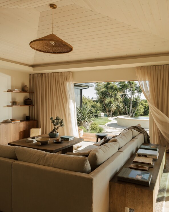 Neutral sectional and wood console in Camille Styles’ family room, framed by a Casa Zuma pendant and garden view.