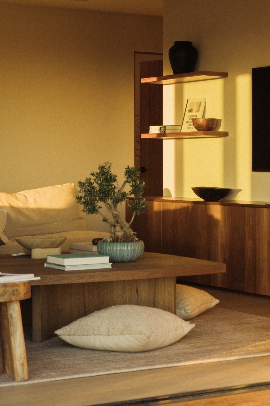 Camille Styles’ family room at dusk with warm wood cabinetry, a low coffee table, ceramics, and floor cushions.