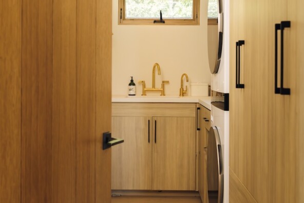 Camille Styles’ narrow Malibu laundry room with warm wood cabinetry, integrated appliances, and a utility sink.