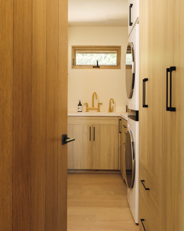 Camille Styles’ narrow Malibu laundry room with warm wood cabinetry, integrated appliances, and a utility sink.