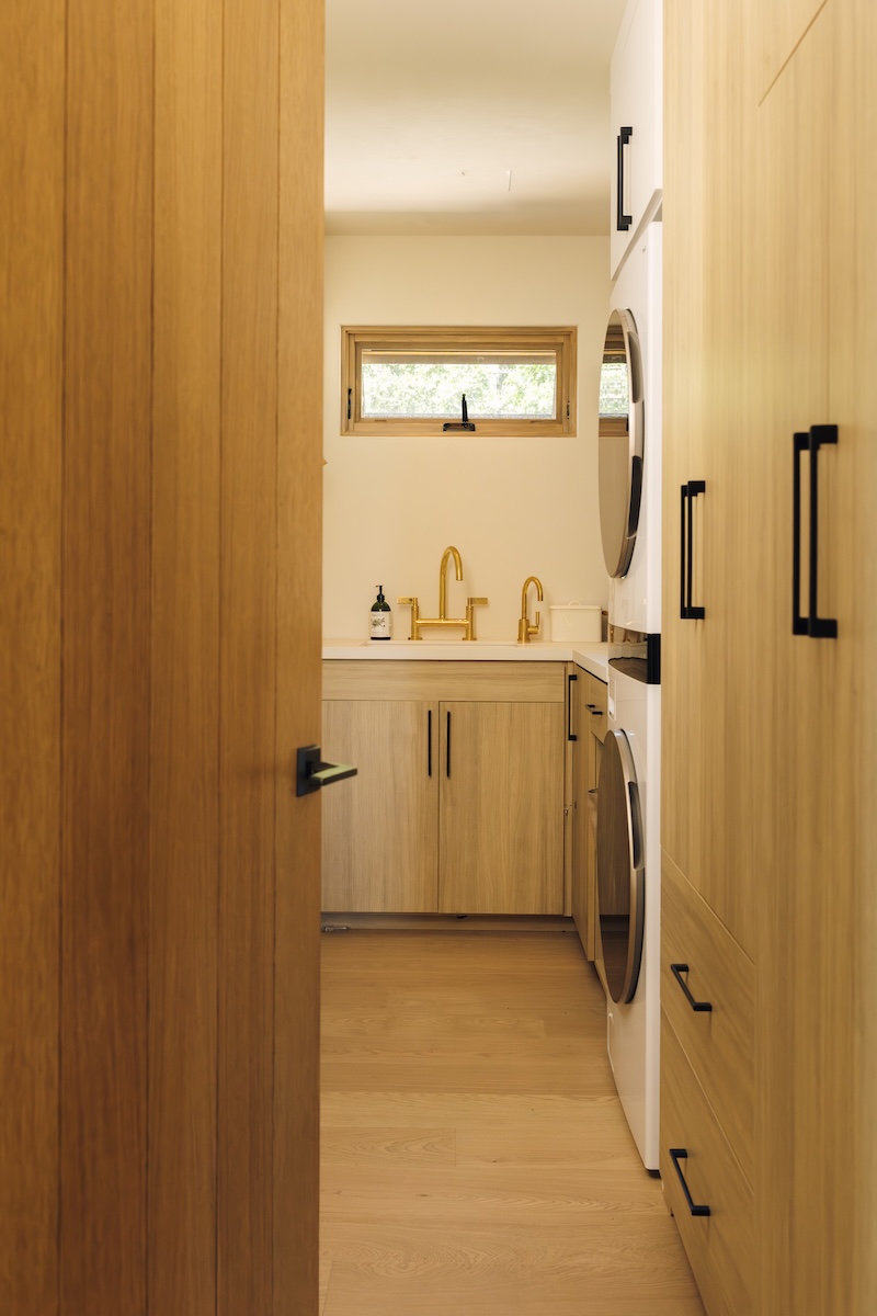 Camille Styles’ narrow Malibu laundry room with warm wood cabinetry, integrated appliances, and a utility sink.