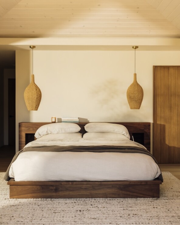 Camille Styles’ Malibu bedroom with a low wood bed, neutral linen bedding, and woven pendant lights.