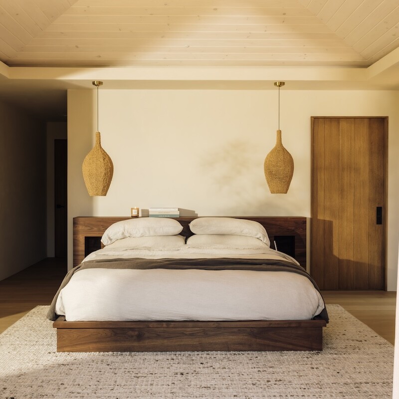 Camille Styles’ Malibu bedroom with a low wood bed, neutral linen bedding, and woven pendant lights.