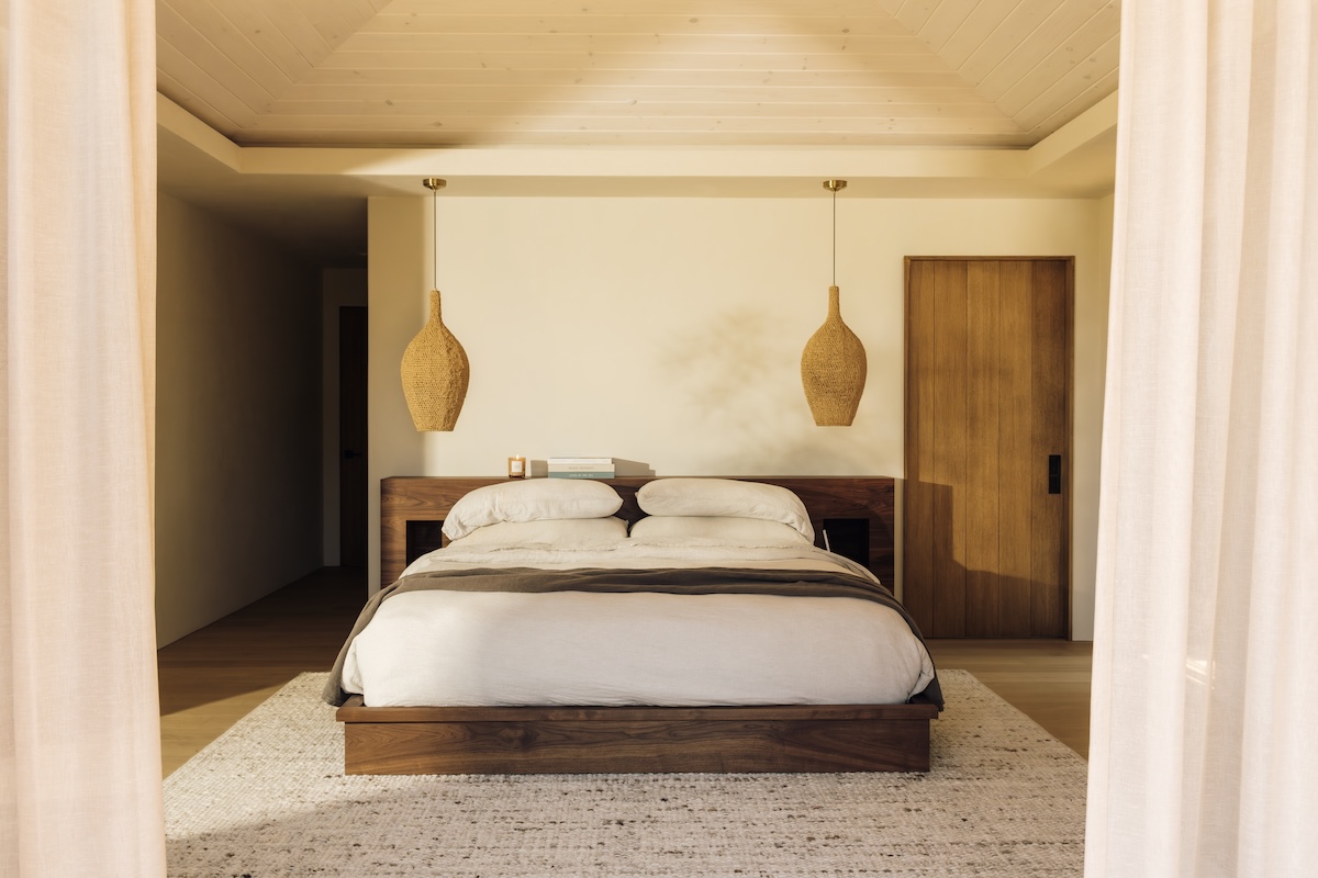 Camille Styles’ Malibu bedroom with a low wood bed, neutral linen bedding, and woven pendant lights.