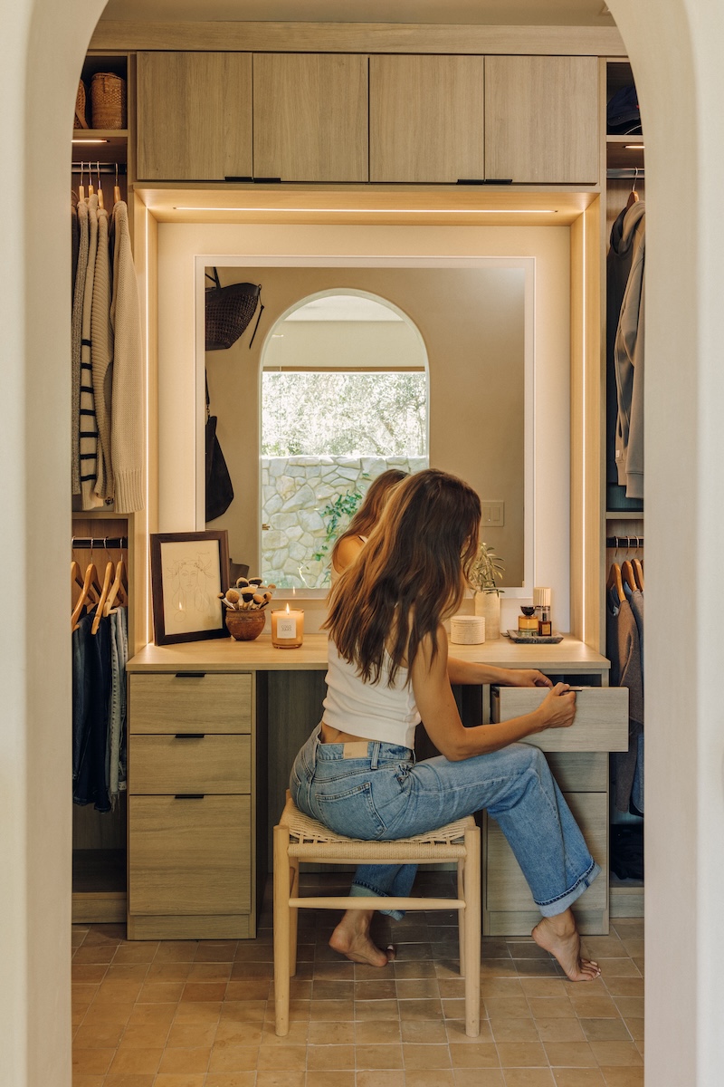 Camille Styles seated at the built-in vanity in her warm wood walk-in closet.