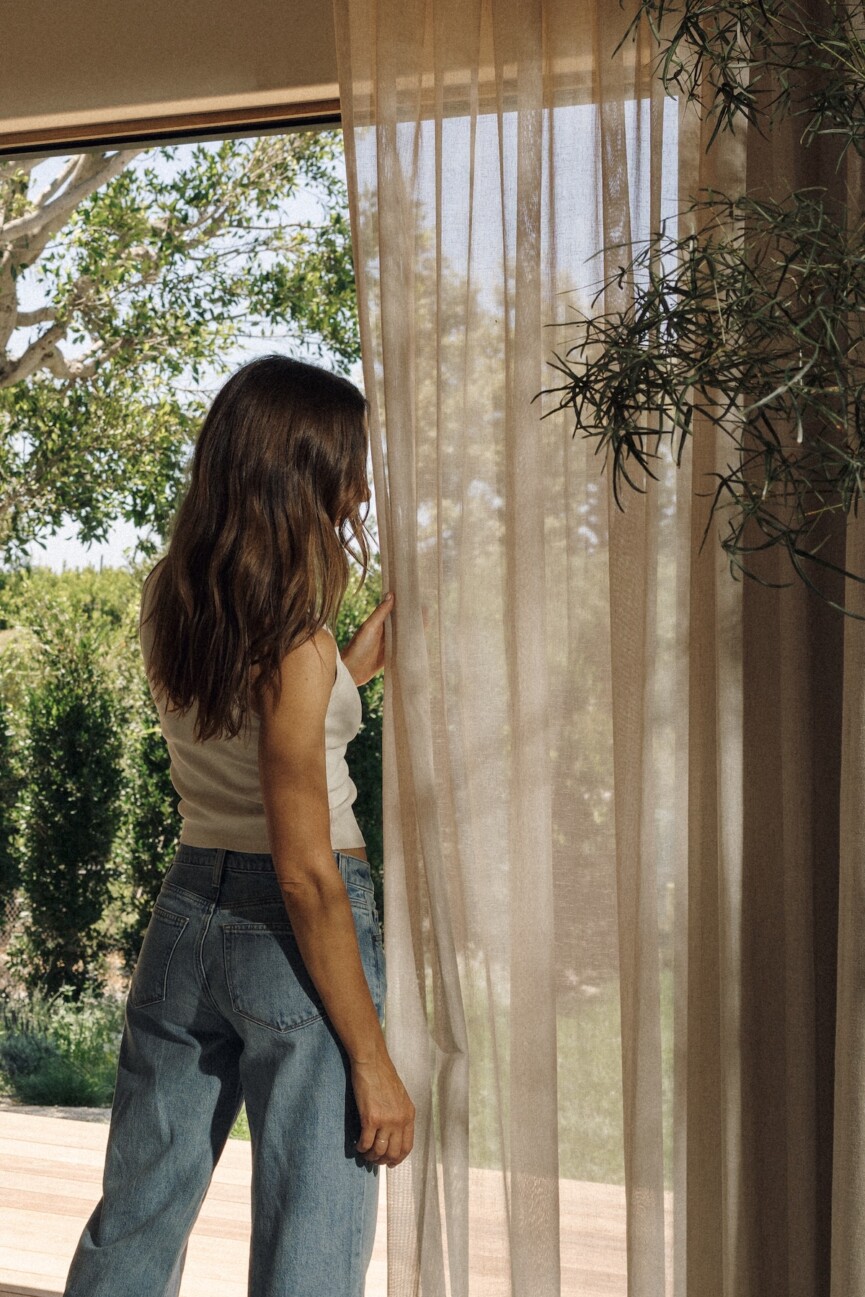 Camille Styles opens sheer curtains overlooking the garden at her Malibu home.