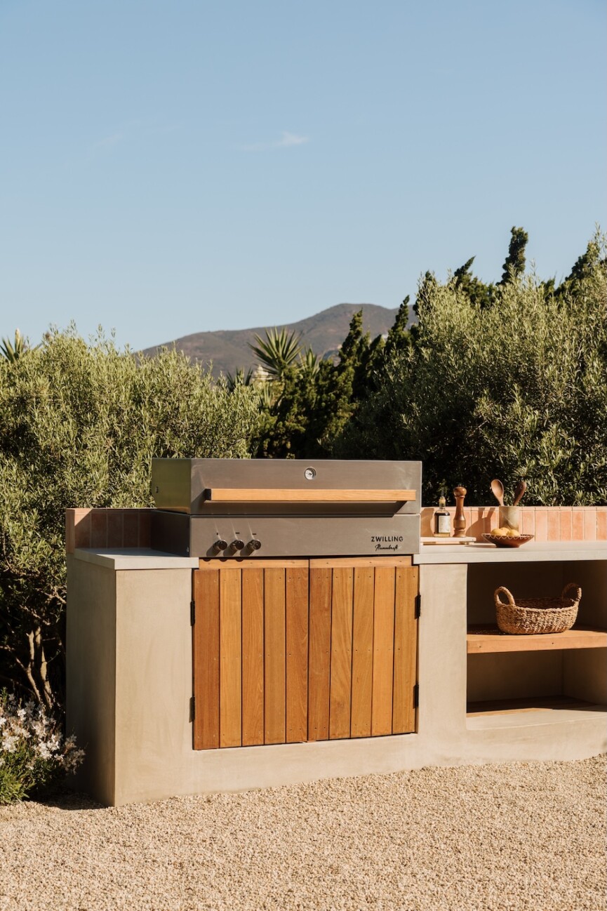 Built-in stainless steel grill with wood cabinetry and open shelving in Camille Styles’ outdoor kitchen.