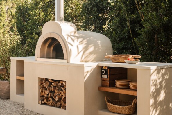 Built-in wood-fired pizza oven with open shelving and firewood storage in the Malibu outdoor kitchen.