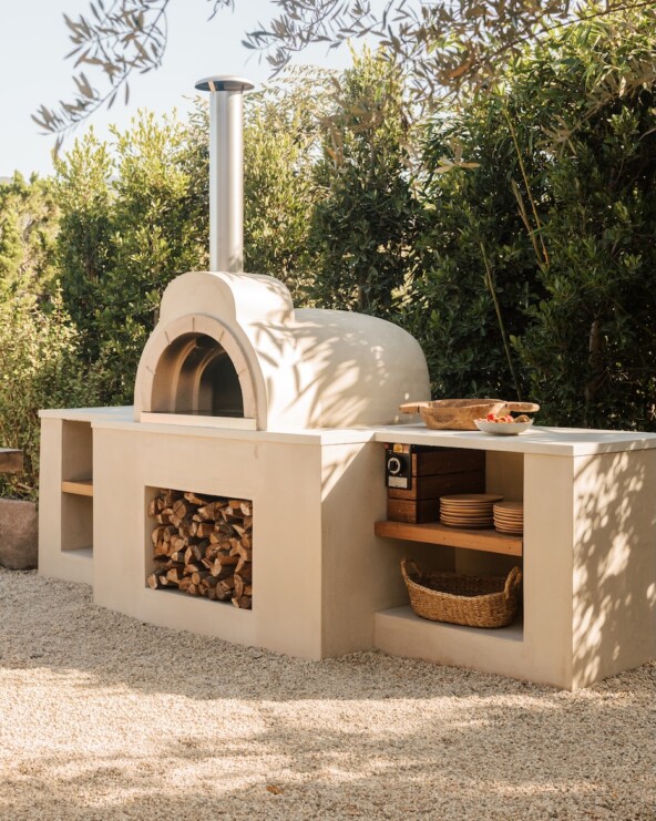 Built-in wood-fired pizza oven with open shelving and firewood storage in the Malibu outdoor kitchen.