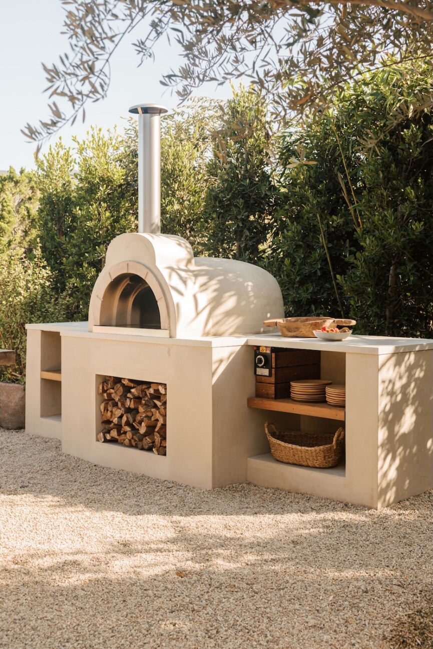 Built-in wood-fired pizza oven with open shelving and firewood storage in the Malibu outdoor kitchen.