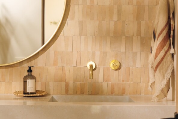 Powder bathroom vanity with warm tile, a round mirror, integrated sink, and wall-mounted brass fixtures.