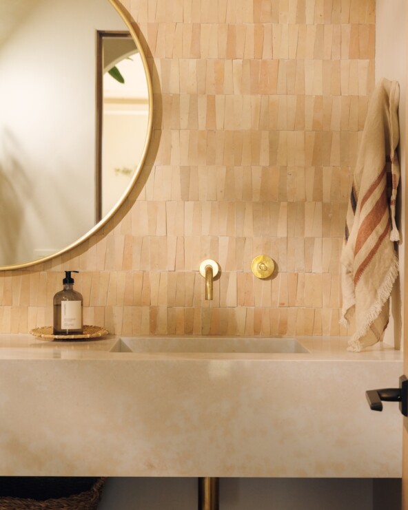 Powder bathroom vanity with warm tile, a round mirror, integrated sink, and wall-mounted brass fixtures.