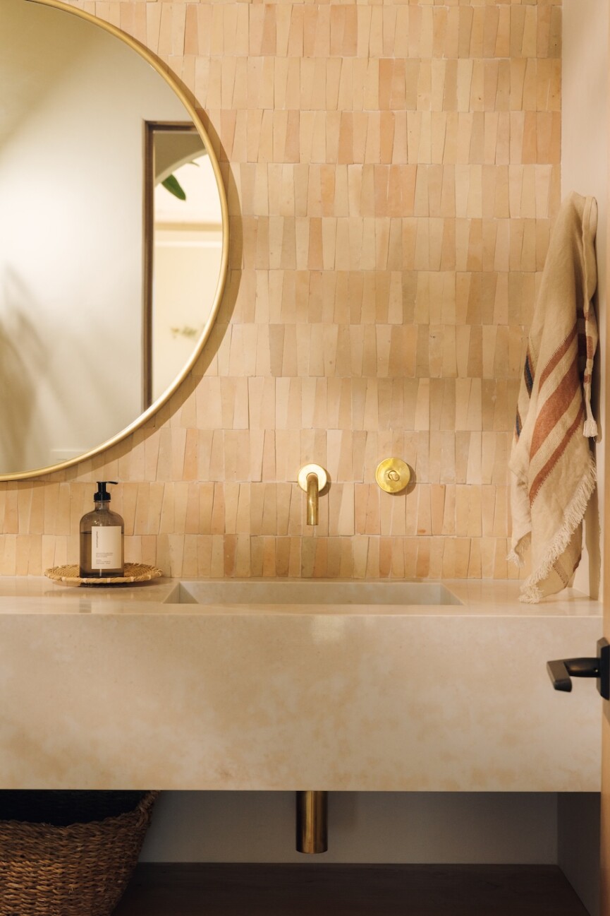 Powder bathroom vanity with warm tile, a round mirror, integrated sink, and wall-mounted brass fixtures.