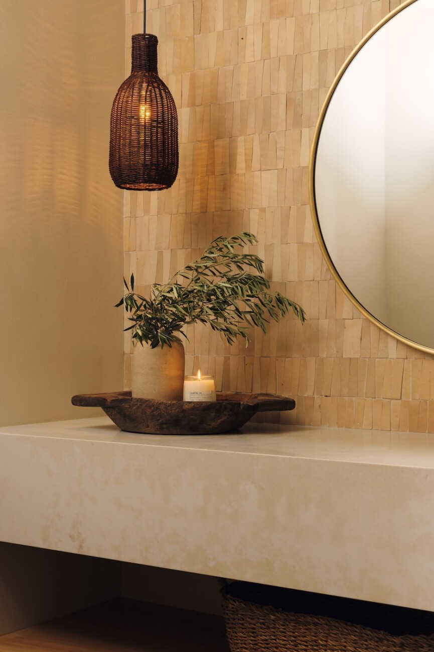 Floating stone vanity styled with greenery and a candle beneath an amber glass pendant light.