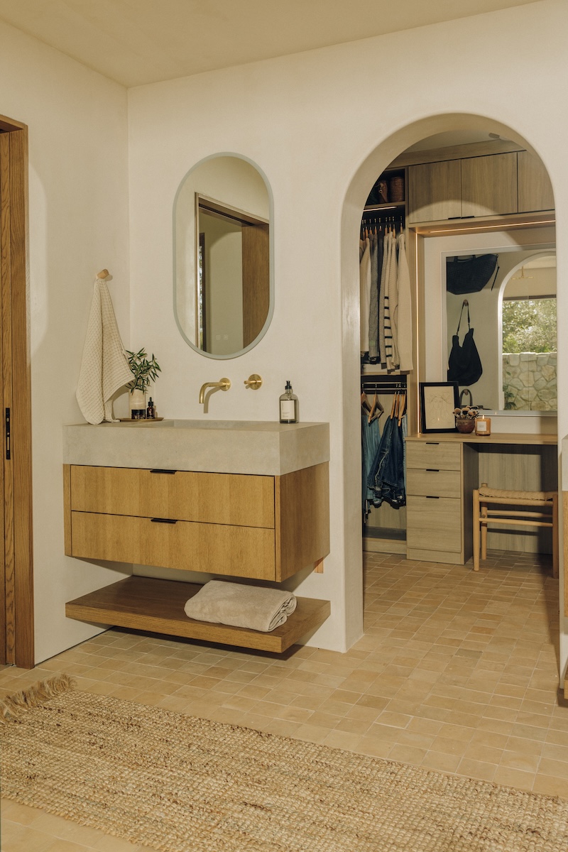 Floating wood vanity with an arched mirror beside the entrance to Camille Styles’ walk-in closet.