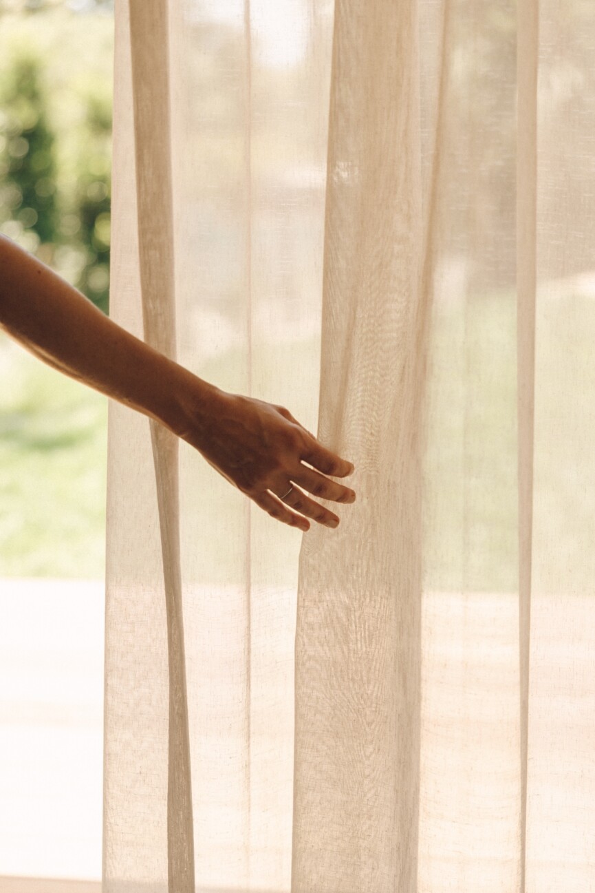 Close-up of a hand touching the textured sheer curtains in Camille Styles’ Malibu home.
